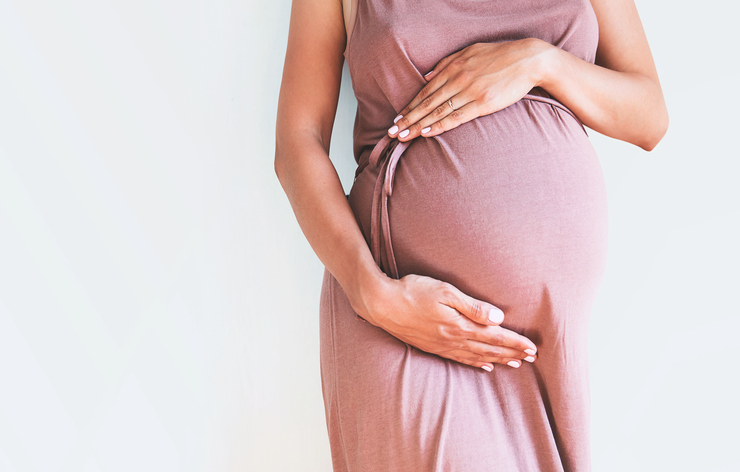 Pregnant woman in dress holds hands on belly on a white background. Pregnancy, maternity, preparation and expectation concept. Close-up, copy space, indoors. Beautiful tender mood photo of pregnancy.